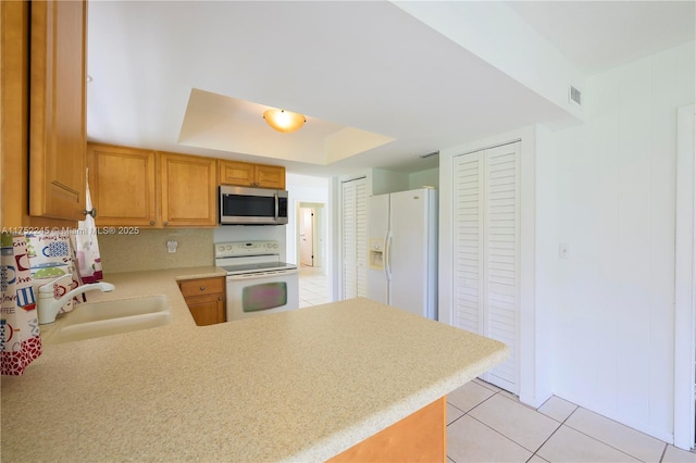 kitchen featuring white appliances, a raised ceiling, a peninsula, light countertops, and a sink