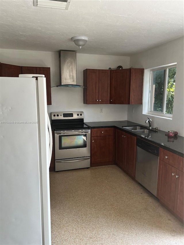 kitchen with appliances with stainless steel finishes, dark countertops, a sink, and wall chimney range hood