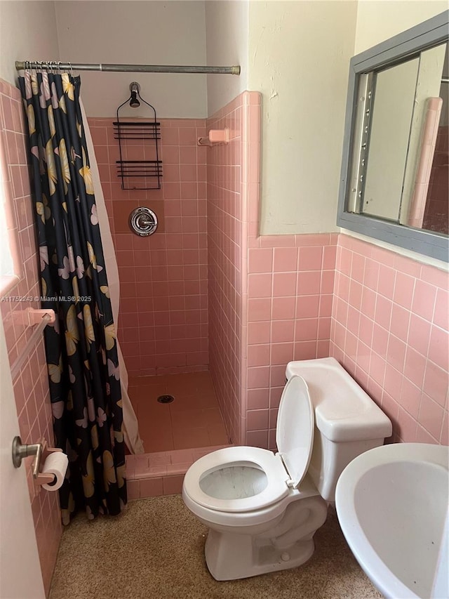 bathroom with wainscoting, toilet, a tile shower, speckled floor, and tile walls