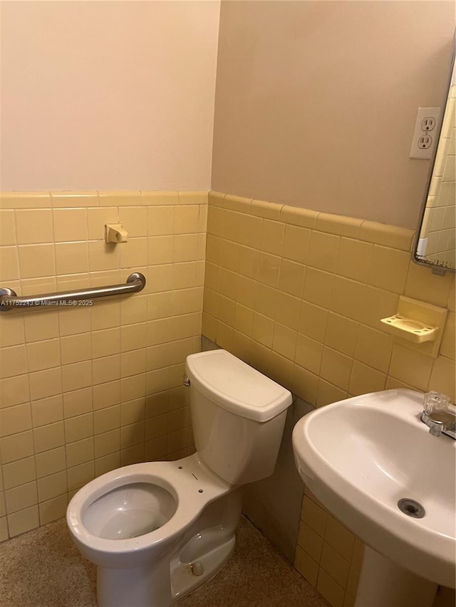 bathroom with toilet, tile walls, a sink, and wainscoting