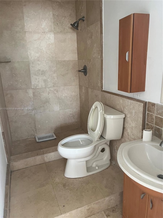 full bathroom with visible vents, tiled shower, vanity, and toilet