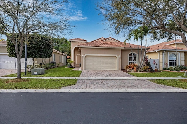 mediterranean / spanish-style home with decorative driveway, a tile roof, stucco siding, an attached garage, and a front lawn