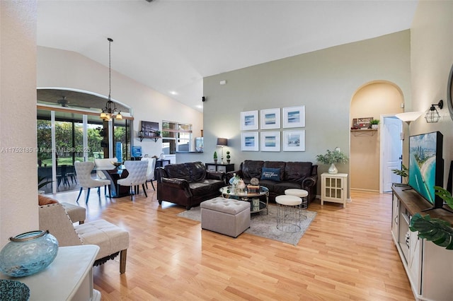 living room featuring an inviting chandelier, light wood-style flooring, high vaulted ceiling, and arched walkways