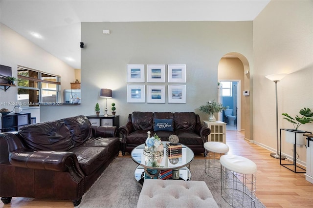 living area with arched walkways, high vaulted ceiling, light wood-type flooring, and baseboards