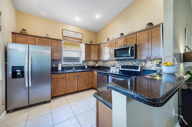 kitchen with lofted ceiling, a peninsula, appliances with stainless steel finishes, dark stone counters, and brown cabinetry