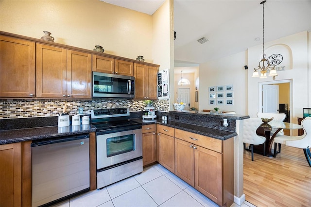 kitchen with brown cabinets, decorative light fixtures, visible vents, appliances with stainless steel finishes, and dark stone counters