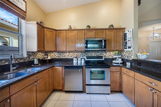 kitchen featuring light tile patterned floors, appliances with stainless steel finishes, brown cabinetry, and a sink