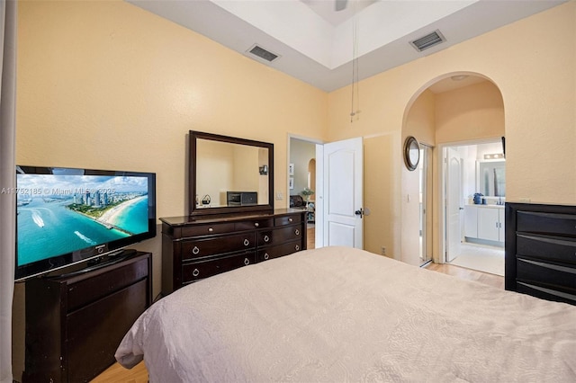 bedroom with arched walkways, light wood finished floors, ensuite bath, and visible vents