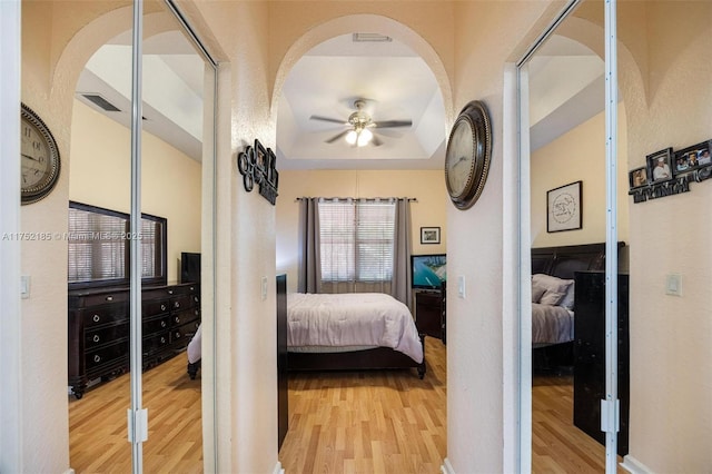 bedroom with light wood-type flooring, visible vents, a textured wall, and a tray ceiling