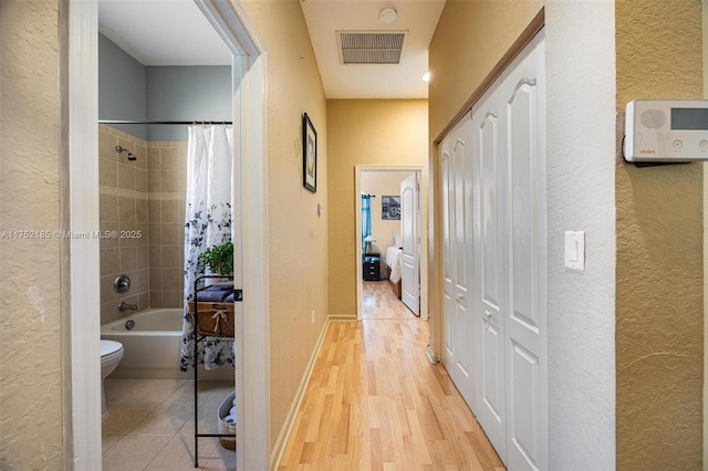 hall with baseboards, visible vents, light wood-style flooring, and a textured wall