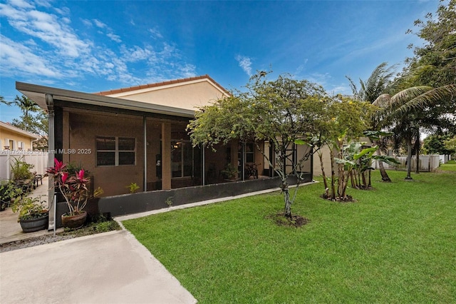 back of house with stucco siding, fence, a sunroom, and a yard