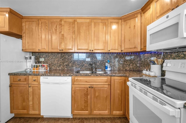 kitchen with decorative backsplash, brown cabinetry, a sink, dark stone countertops, and white appliances