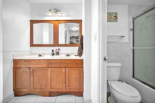 bathroom featuring toilet, double vanity, a sink, and tile walls