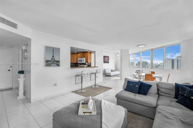 living area with light tile patterned floors, a city view, a ceiling fan, baseboards, and visible vents