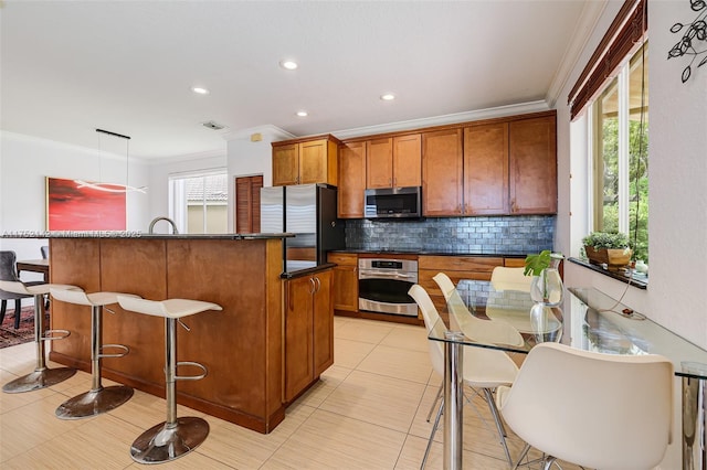 kitchen with stainless steel appliances, an island with sink, dark countertops, decorative light fixtures, and crown molding