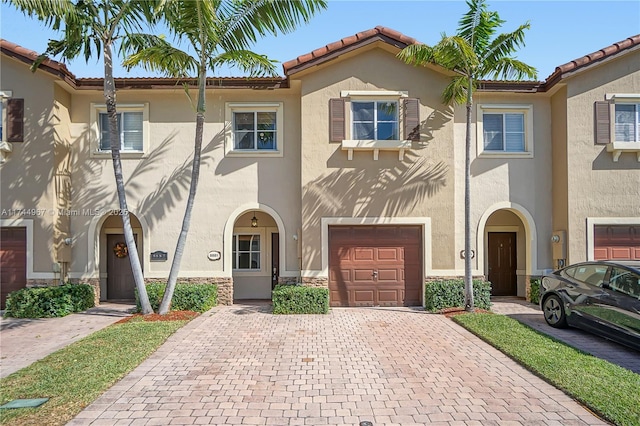 view of front of house with an attached garage, a tiled roof, stone siding, decorative driveway, and stucco siding