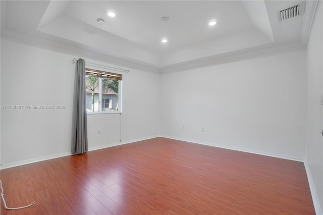 spare room featuring visible vents, baseboards, a raised ceiling, and wood finished floors