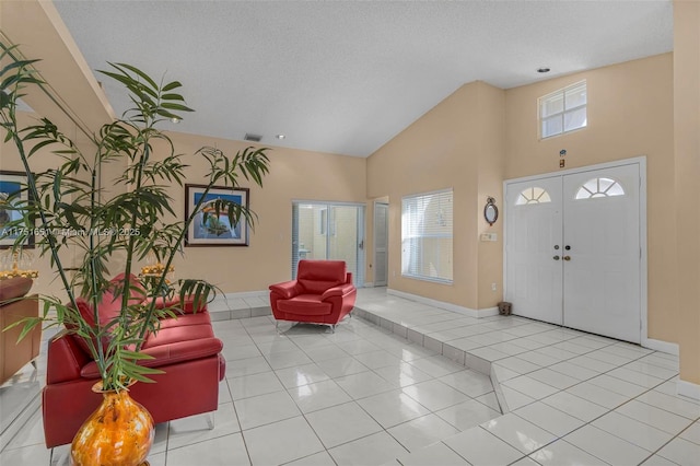 foyer entrance with a textured ceiling, high vaulted ceiling, light tile patterned flooring, visible vents, and baseboards