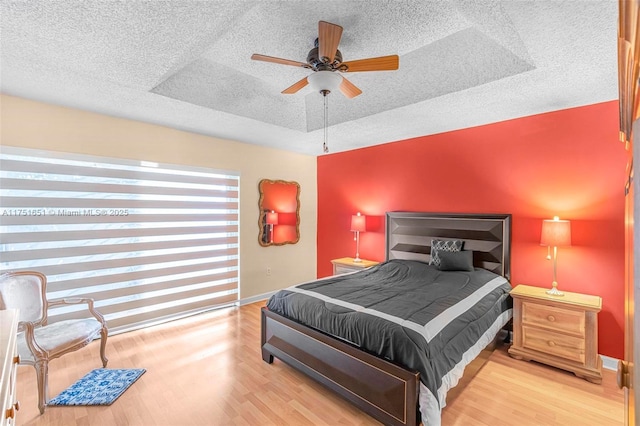 bedroom with a tray ceiling, a textured ceiling, baseboards, and wood finished floors