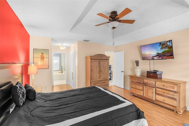 bedroom featuring a textured ceiling, connected bathroom, a ceiling fan, visible vents, and light wood-style floors