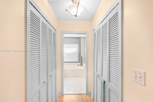 hallway with a textured ceiling and light wood-style floors