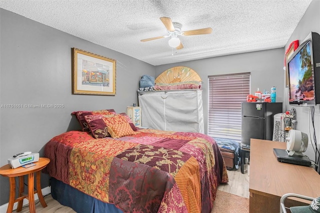 bedroom with a ceiling fan, light wood-type flooring, freestanding refrigerator, and a textured ceiling