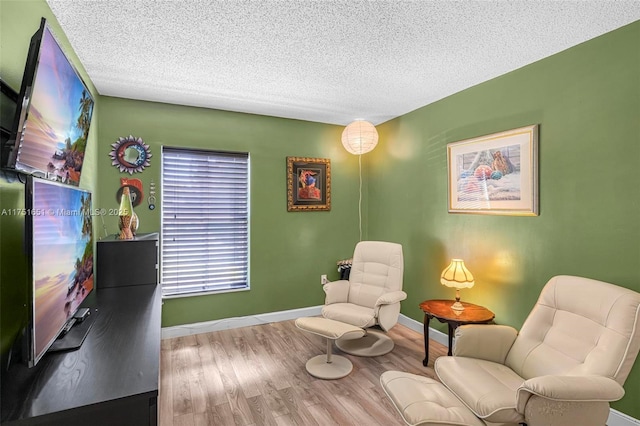 living area with baseboards, a textured ceiling, and light wood finished floors