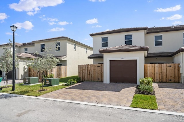 view of front facade featuring decorative driveway, stucco siding, fence, a garage, and a tiled roof