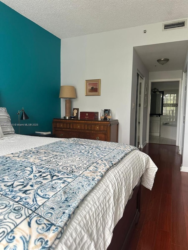 bedroom with dark wood-style floors, baseboards, visible vents, and a textured ceiling