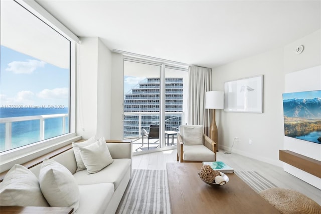 living room with a water view, light wood finished floors, expansive windows, and baseboards