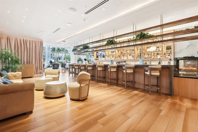 interior space with a wall of windows, indoor wet bar, visible vents, and light wood-style floors