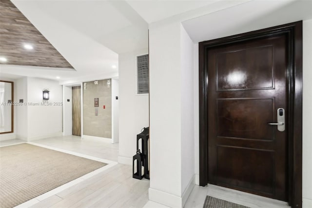 hallway with baseboards, light wood finished floors, elevator, and recessed lighting