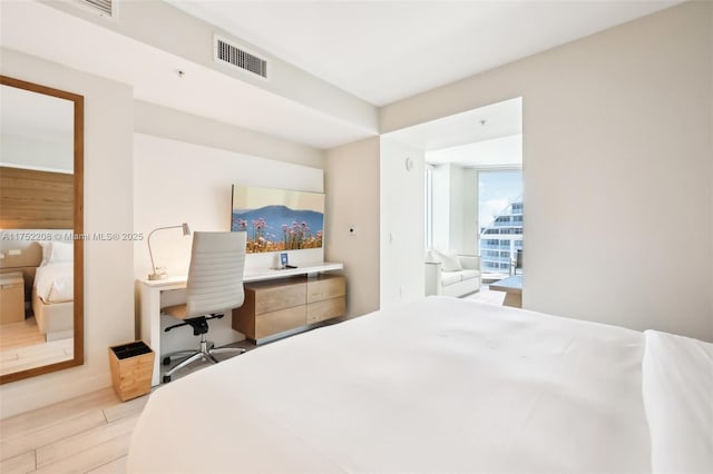 bedroom with light wood finished floors, visible vents, and built in study area