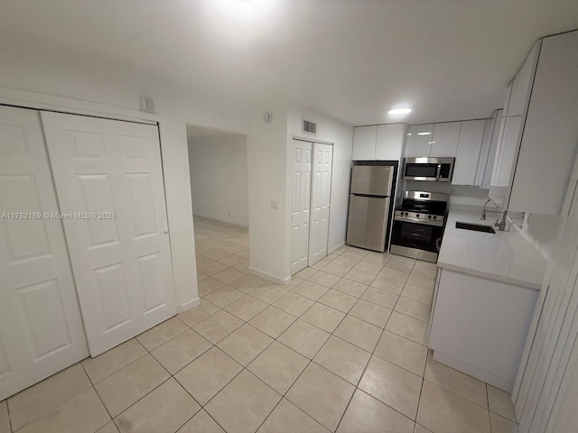 kitchen featuring light tile patterned floors, appliances with stainless steel finishes, light countertops, white cabinetry, and a sink