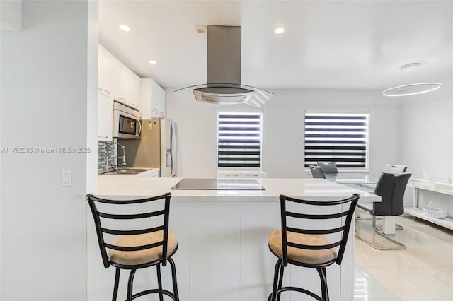 kitchen featuring appliances with stainless steel finishes, a peninsula, island exhaust hood, light countertops, and white cabinetry