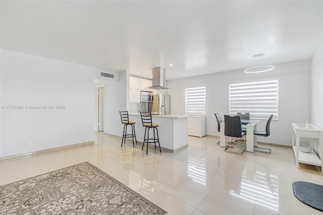 kitchen with a breakfast bar area, stainless steel appliances, a peninsula, visible vents, and white cabinets