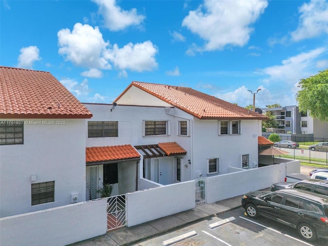 exterior space featuring a fenced front yard, a tile roof, uncovered parking, and stucco siding