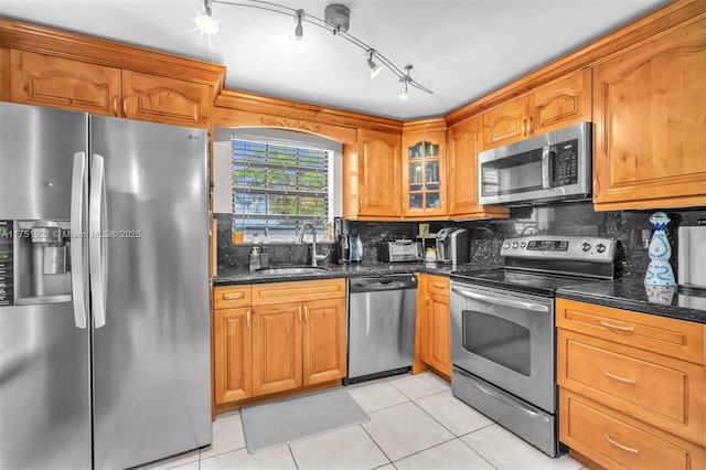 kitchen with light tile patterned floors, glass insert cabinets, dark stone countertops, stainless steel appliances, and a sink