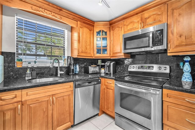 kitchen featuring stainless steel appliances, dark stone countertops, a sink, and glass insert cabinets