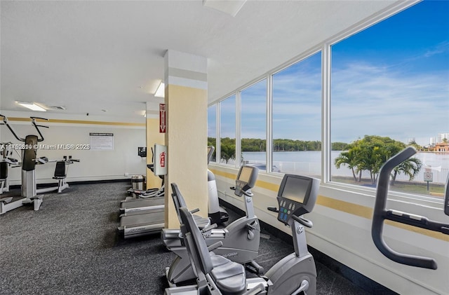 exercise room featuring a water view and baseboards