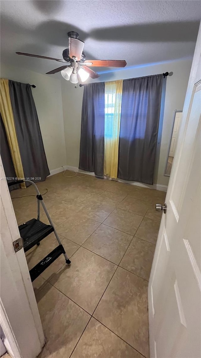 tiled empty room with ceiling fan, baseboards, and a textured ceiling