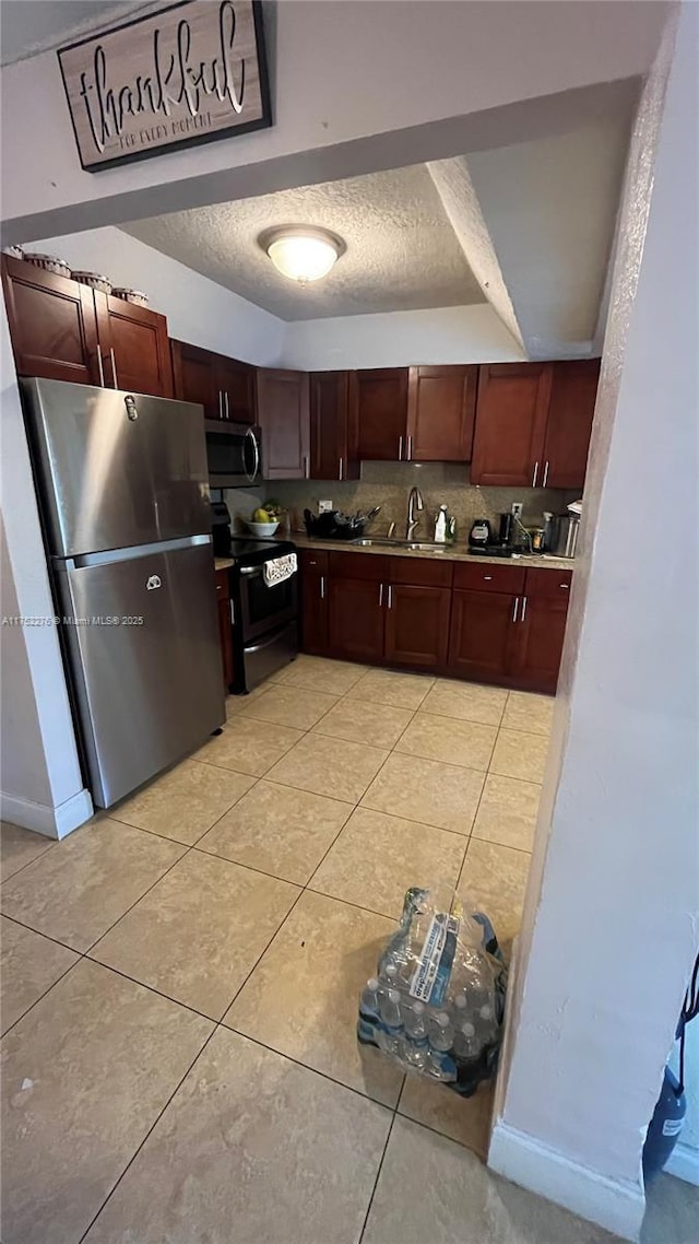 kitchen with light tile patterned floors, decorative backsplash, appliances with stainless steel finishes, a textured ceiling, and a sink