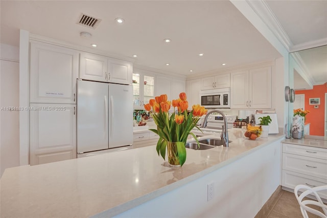 kitchen featuring a peninsula, white appliances, a sink, visible vents, and white cabinetry