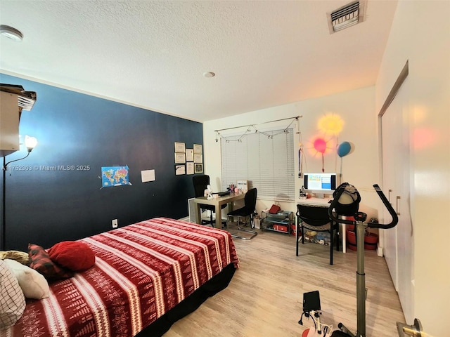 bedroom with visible vents, light wood finished floors, and a textured ceiling