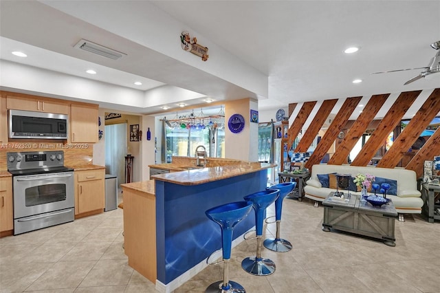 kitchen with visible vents, appliances with stainless steel finishes, open floor plan, a kitchen bar, and a sink