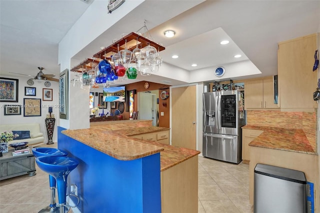 kitchen featuring stainless steel refrigerator with ice dispenser, light tile patterned floors, open floor plan, a peninsula, and a kitchen breakfast bar