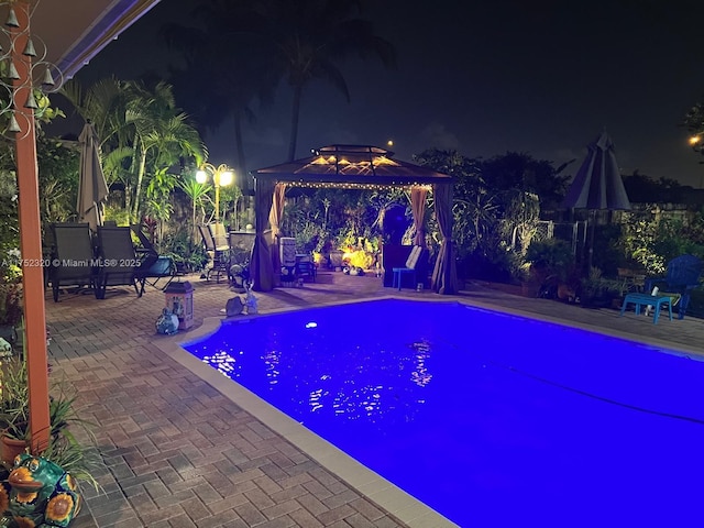 pool at night featuring a gazebo, a patio area, and an outdoor pool