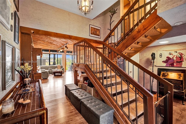 stairs with a high ceiling, wood finished floors, and an inviting chandelier