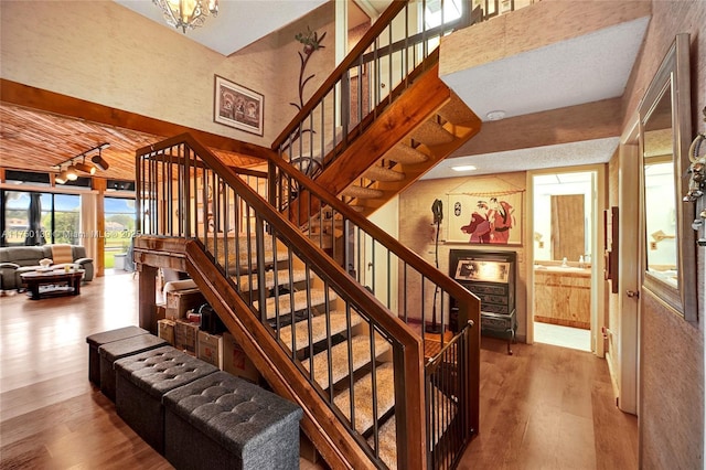 staircase with a towering ceiling, track lighting, and wood finished floors