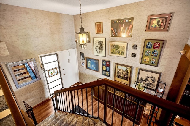 staircase with a towering ceiling, wallpapered walls, and wood finished floors